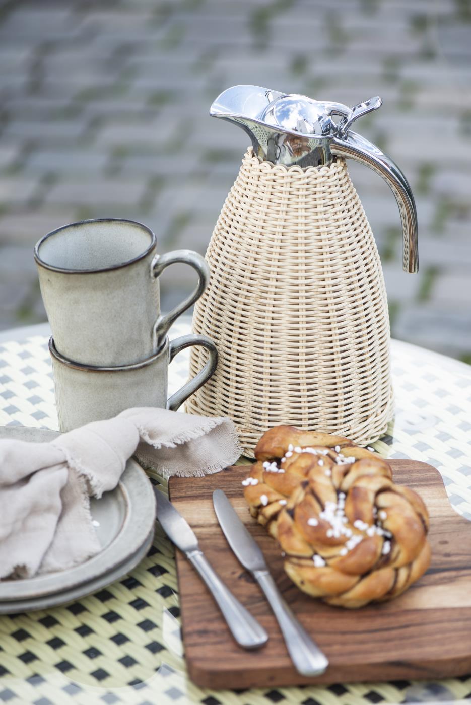 Flätad termoskanna från Ib Laursen på utomhuskaffebord med keramikmuggar, en croissant och rustikt servis.