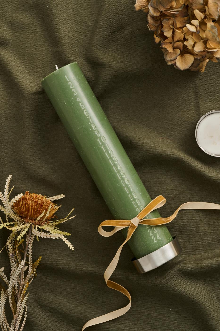 Gyllene clayfärgat velourband bundet som rosett runt ett grönt ljus med torkade blommor och naturpynt