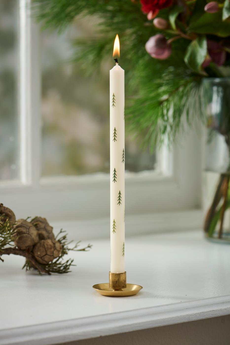 Mässingsljusstake med vitt kronljus med gröna motiv i en julpyntad fönsterkarm