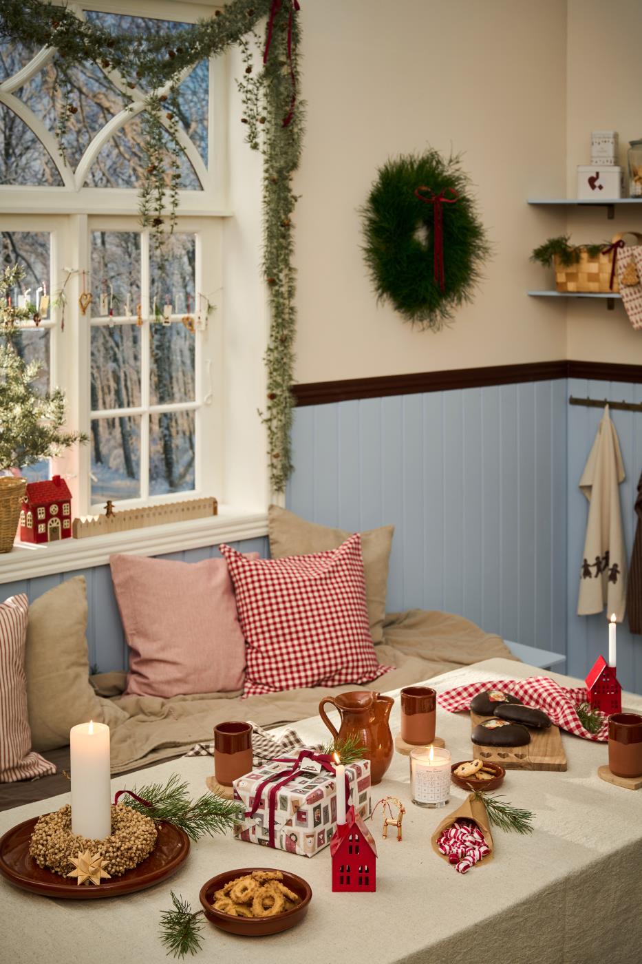 Linnefärgad duk på ett bord med julklappar, gran, röda detaljer och julpynt i ett mysigt vardagsrum