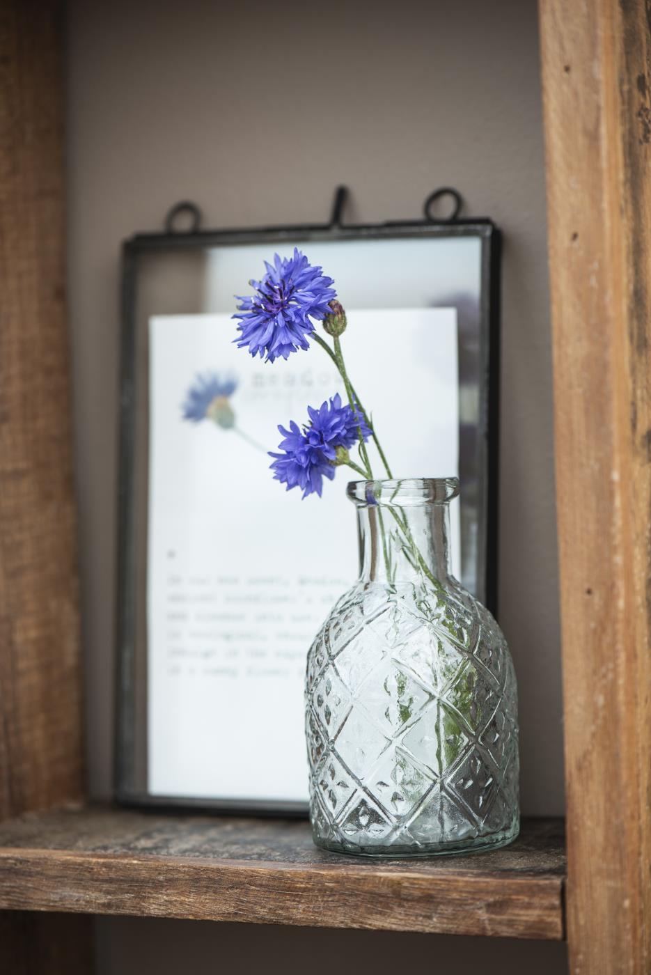 Apotekerglas med harlekinmönster och blå ängsblommor som dekoration på en trähylla