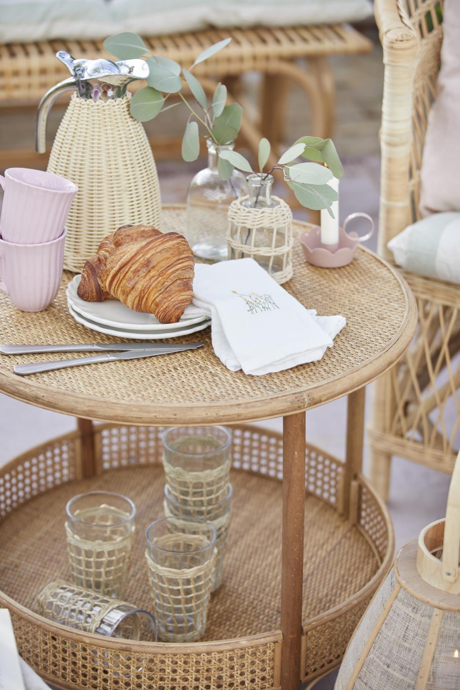 Termoskanna från Ib Laursen på ett runt flätbord med croissant, glas och blommor i en mysig somrig bordsdukning.
