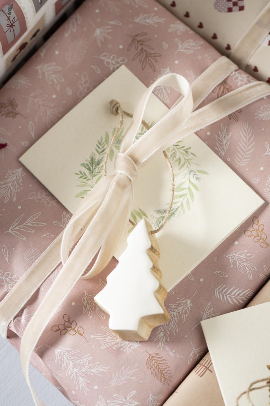 Ljust velourband knutet som en rosett runt en julklapp med naturinspirerat presentpynt