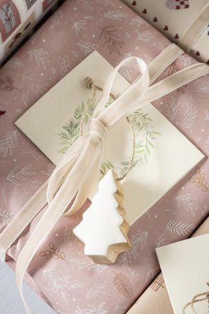 Ljust velourband knutet som en rosett runt en julklapp med naturinspirerat presentpynt