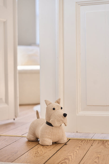 Dörrstoppare i form av en vit och beige skotsk terrier från Speedtsberg som håller upp en vit dörr