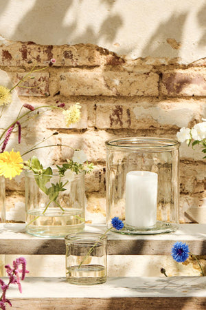 Klart Hannahcylinderglas från Ib Laursen med vitt blockljus bland små glasvaser och blommor