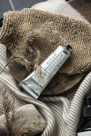 Naturfärgad badhandske i jute tillsammans med vårdande produkter från ALTUM och mjuka handdukar.