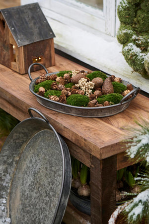 Oval Urban Garden-bricka med mossa, kottar och naturmaterial som vinterdekoration på ett träbord