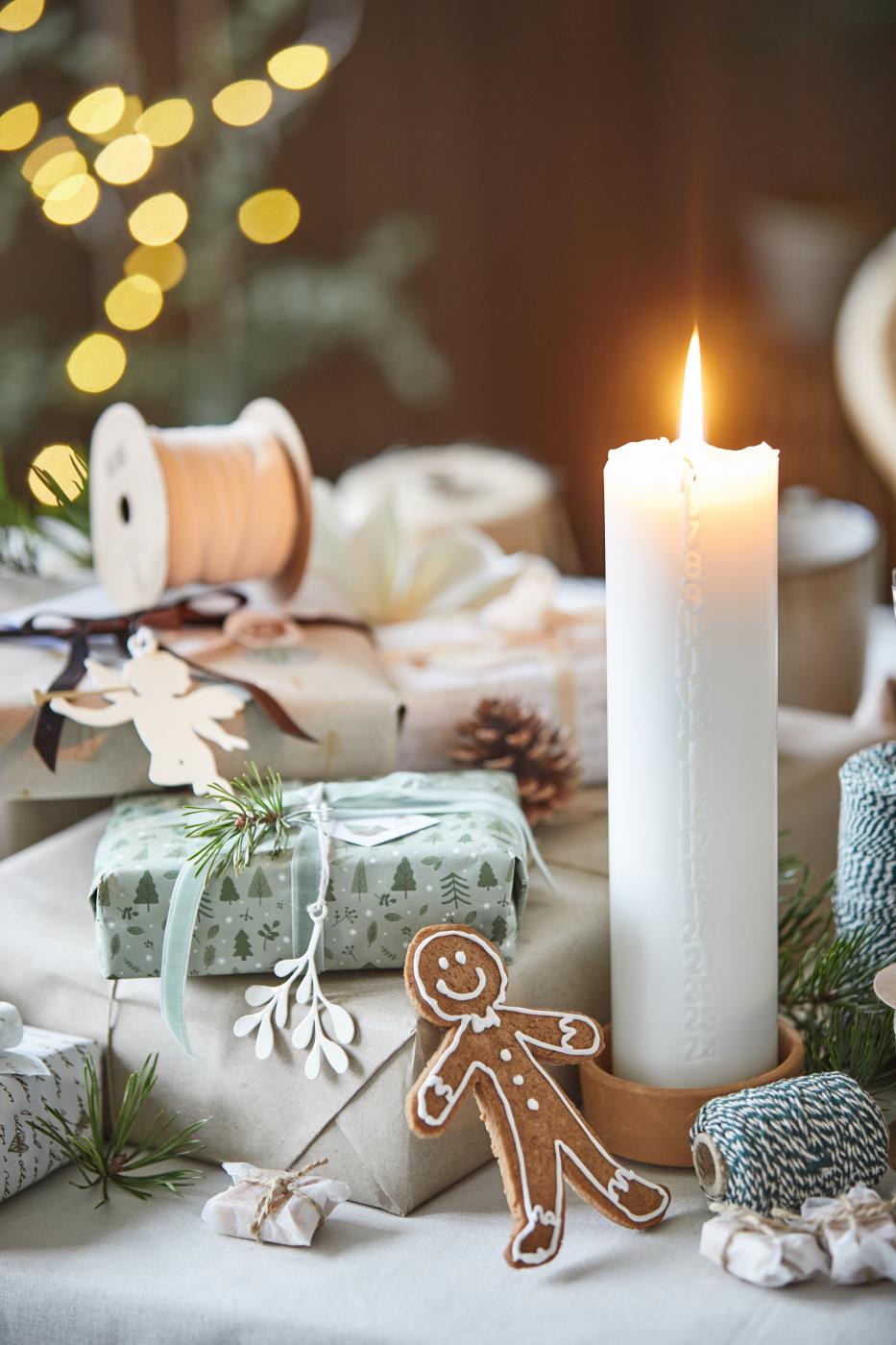 Linfärgad bomullsduk på ett juldekorerat bord med levande ljus, småkakor och inslagna julklappar