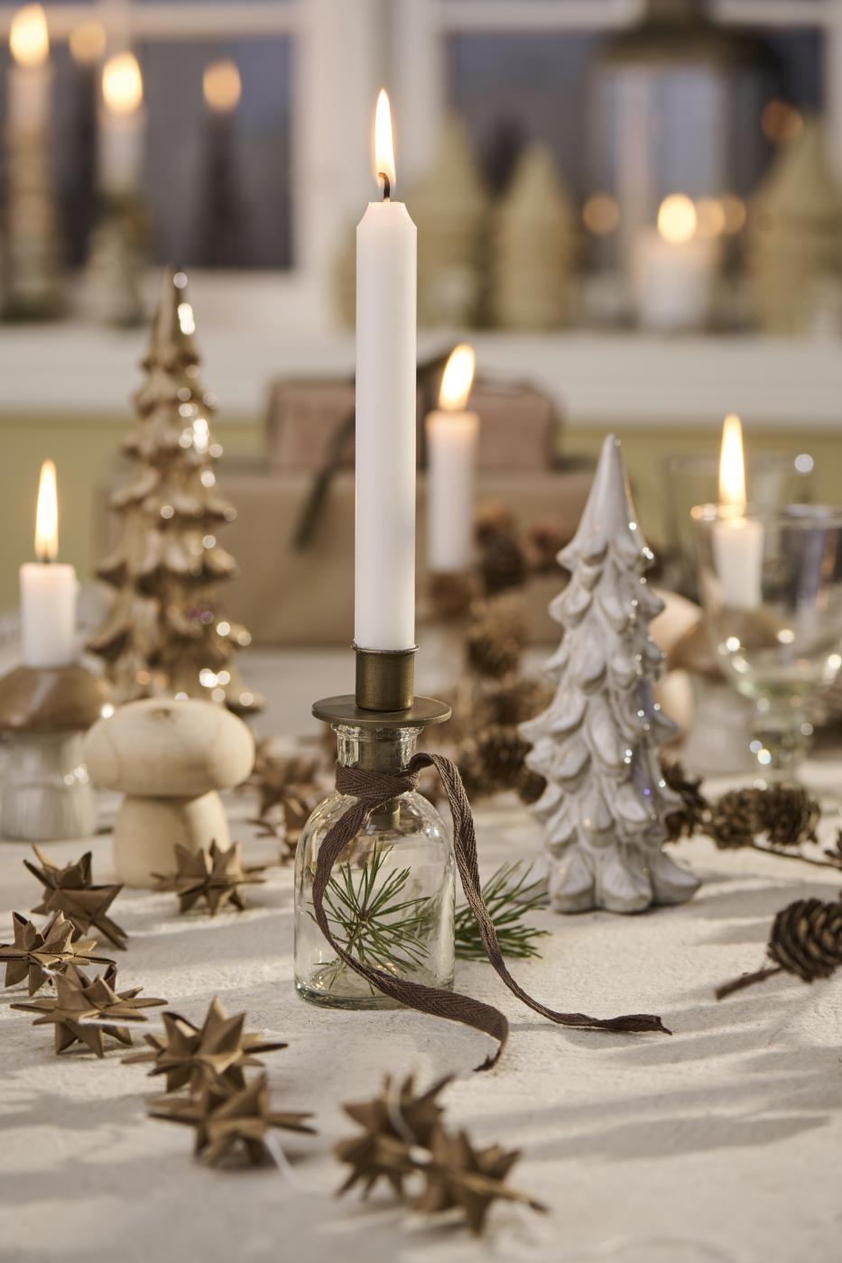 Antika guldfärgade ljusstakar med vita kronljus på ett julbord pyntat med gran, kottar och små julgranar