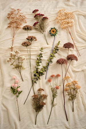 Konstgjorda höstblommor från Ib Laursen i bruna, rosa och gyllene naturfärger arrangerade på ljust tyg.