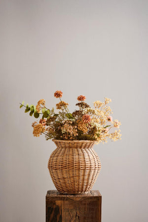 Höstbukett med konstgjord eukalyptus och blommor i gyllene, bruna och krämfärgade nyanser i en flätad vas.