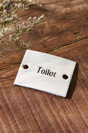 Skilt til toilet i hvid metal ligger på gulv